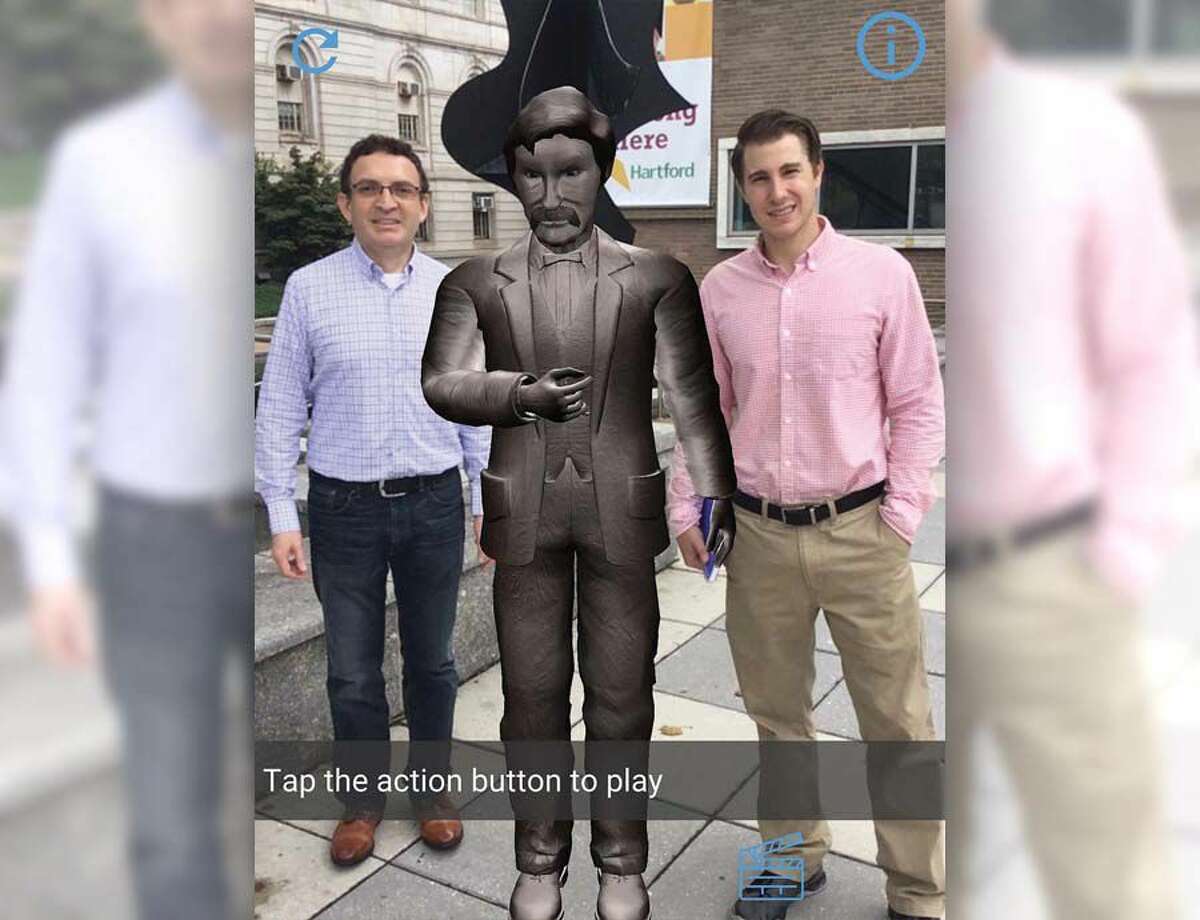 David Oyanadel, left, and Benjamin Williams appear to stand next to a digital statue of Mark Twain outside Hartford Public Library. The illusion is created on smartphones and tablets through the Hey Hartford app developed by Williams’ and Oyanadel’s company ARsome Technology.
