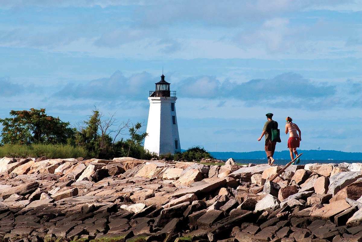 Hikers walk along the jetty toward Black Rock Harbor lighthouse.