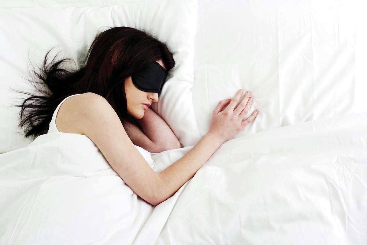 Woman sleeping in a white bed and wearing an eye mask.