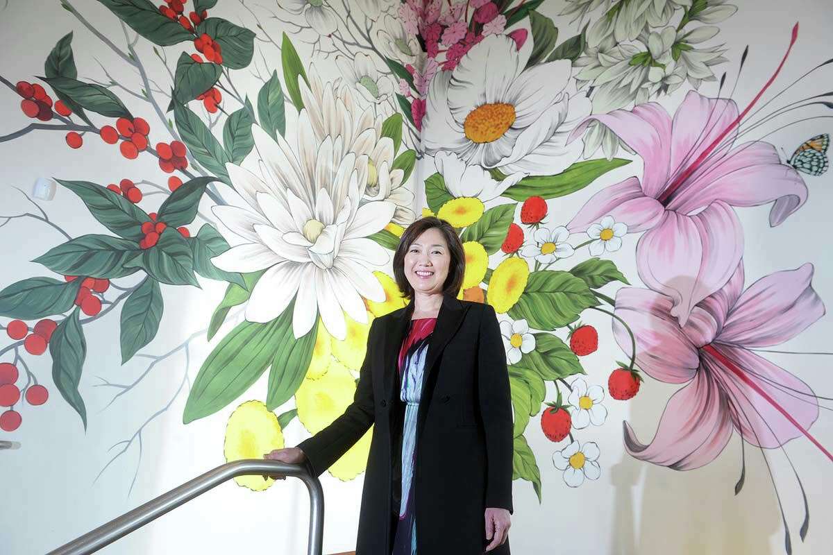 Executive Director Min Jung Kim poses in front of Winter, Spring, Summer, Fall, a site-specific mural painted in 2019 by artist Louise Jones in the main atrium of the New Britain Museum of American Art.
