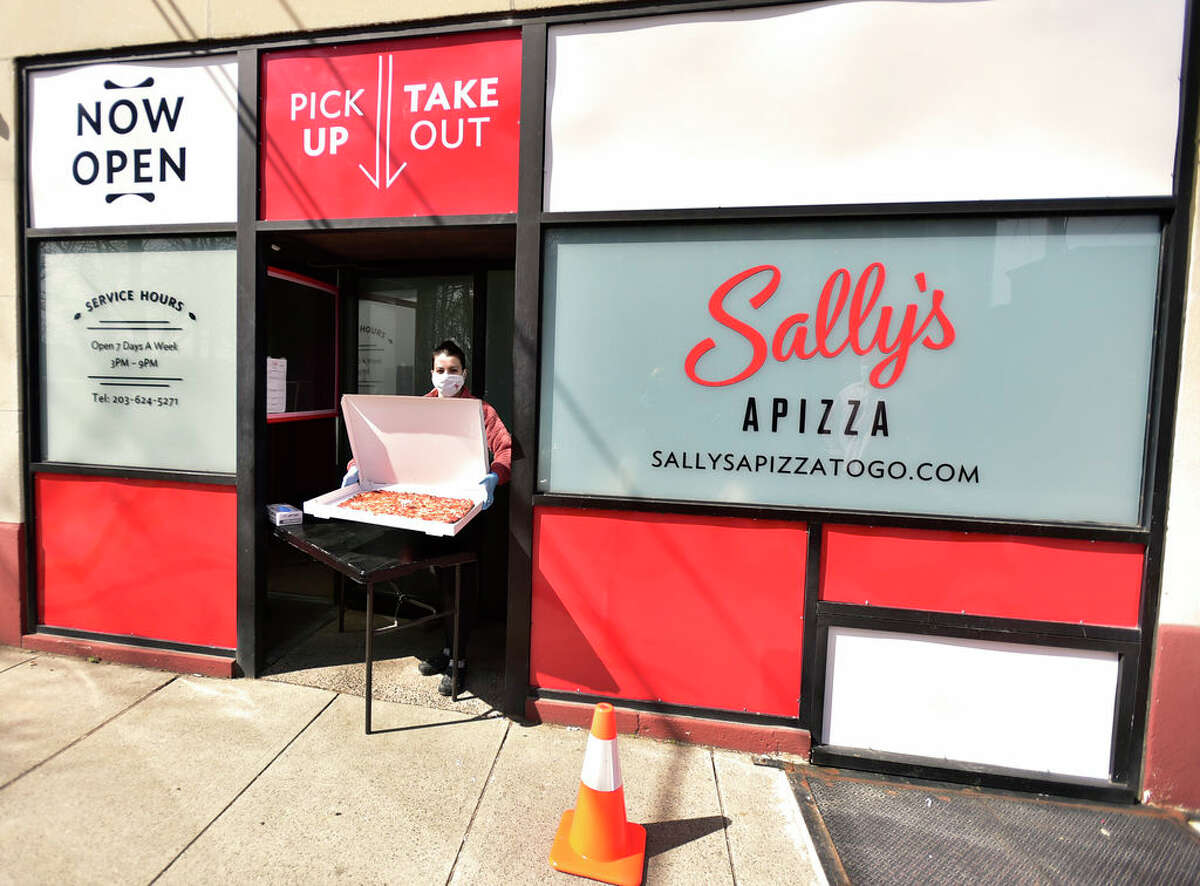 New Haven, Connecticut - Monday, April 20, 2020: Francesca Messina, cashier at Sally's Apizza's shows of a pizza at the pick-up and take-out area at the New Haven pizzeria. Sally's Apizza, which had been closed for several weeks since the state ordered that restaurants only do takeout and delivery, quietly reopened Friday, and later this week, they will do something that Sally's has never done before: getting pizza delivered to your home using online internet delivery services.
