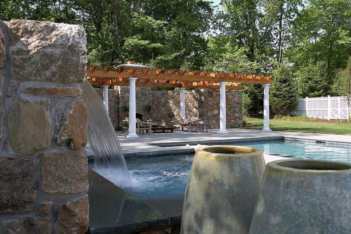 The crown jewel of the outdoor spaces is this pool paradise with a waterfall, fireplace, pergola sitting area, and natural bluestone flatwork and Connecticut fieldstone.