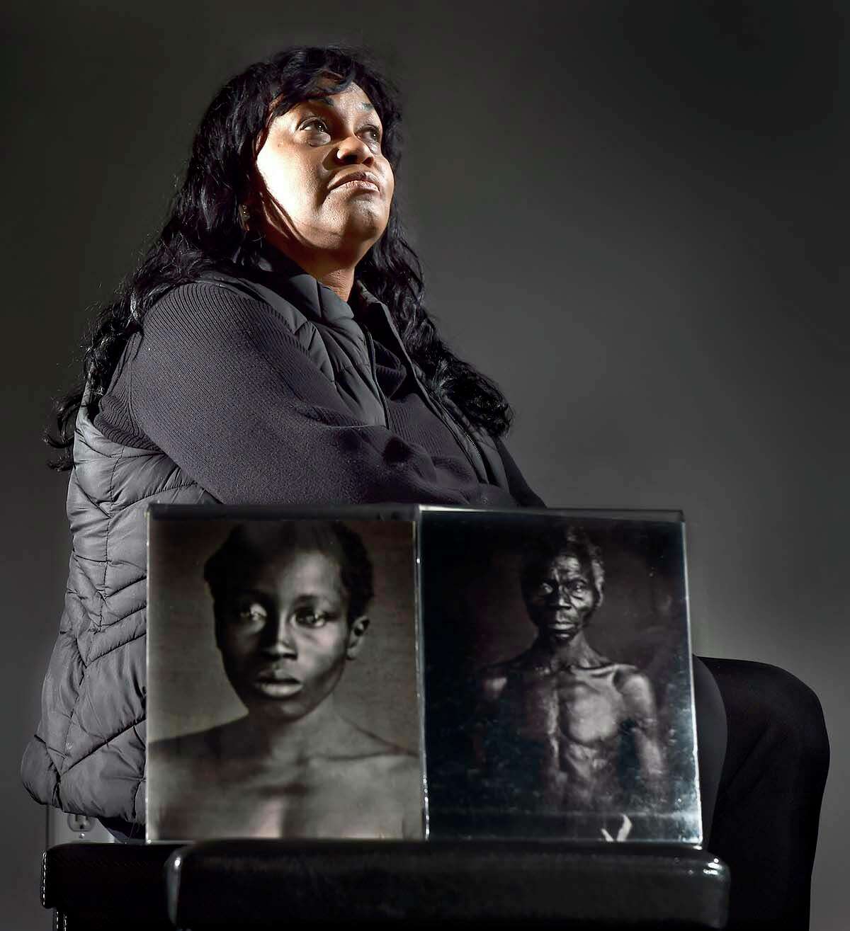 Tamara Lanier, of Norwich, poses with photos of her ancestors Delia Taylor and Renty Taylor.