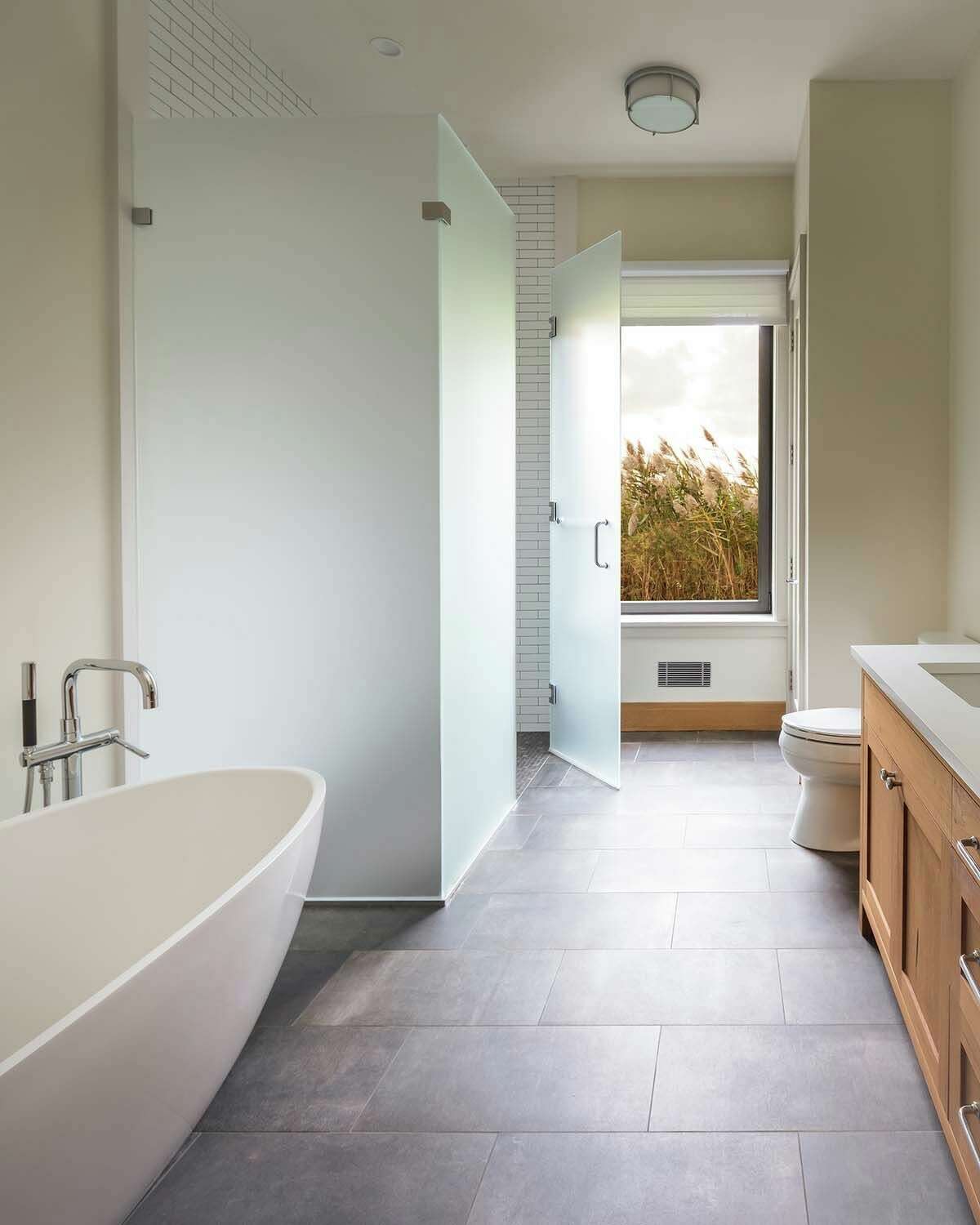 The neutral-toned bathroom, looking out over wind-swept tall reeds, includes a Barcelona soaking tub by Victoria & Albert.