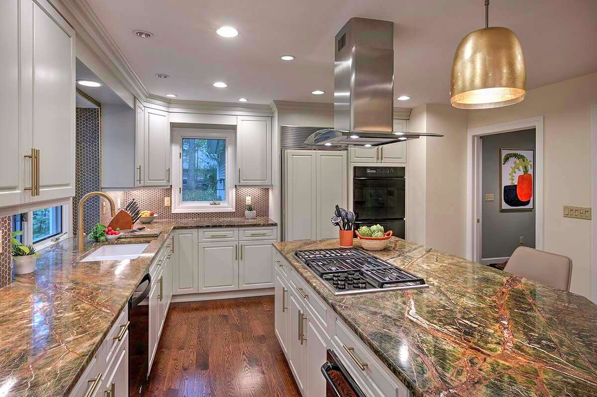 The kitchen contains a copper fireplace hood and brass and golds fixtures. The countertop is rainforest green quartzite, which ties into the overall color scheme.