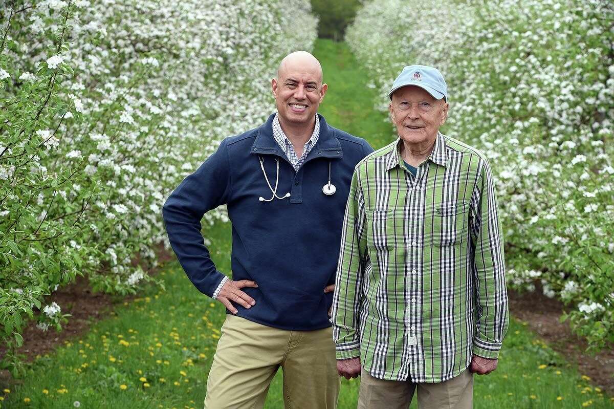 Dr. Julian Nieves, III, photographed with his father, Julian Nieves, Jr., at Lyman Orchards near blooming apple trees in Middlefield.