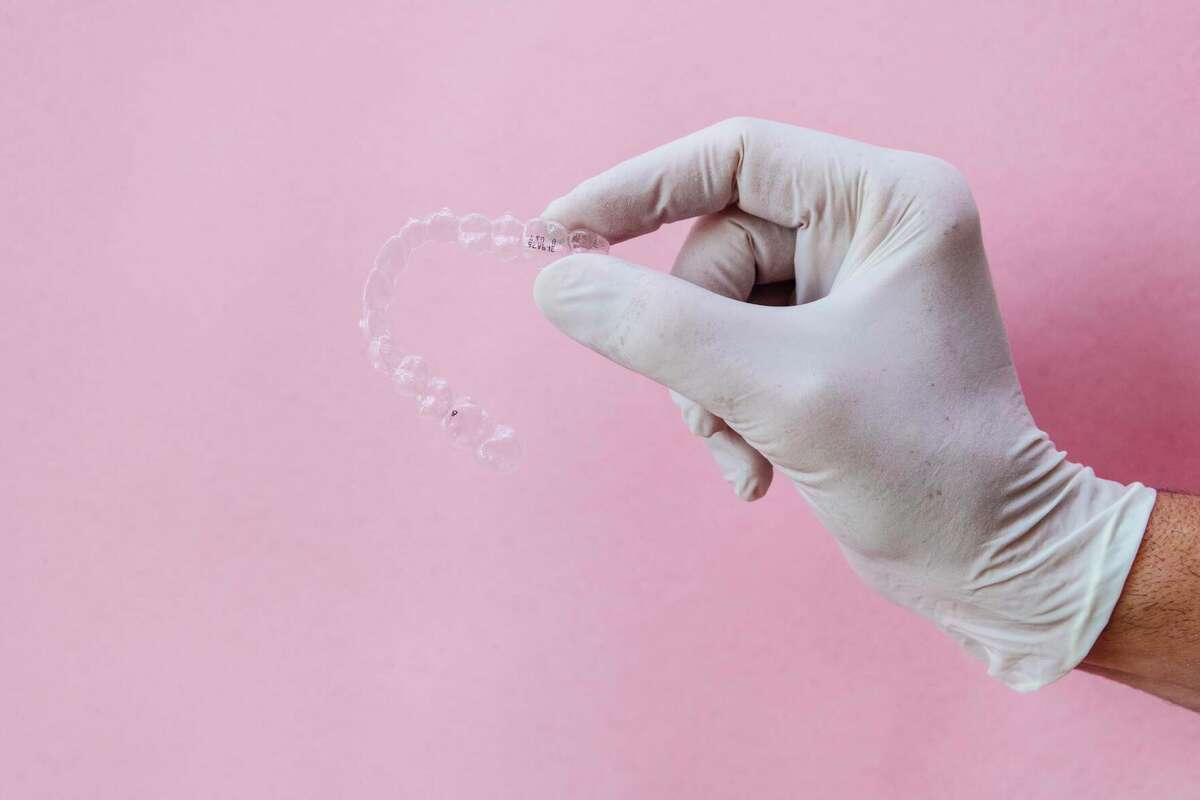 Doctor hand holding a clear dental aligner with the pink background