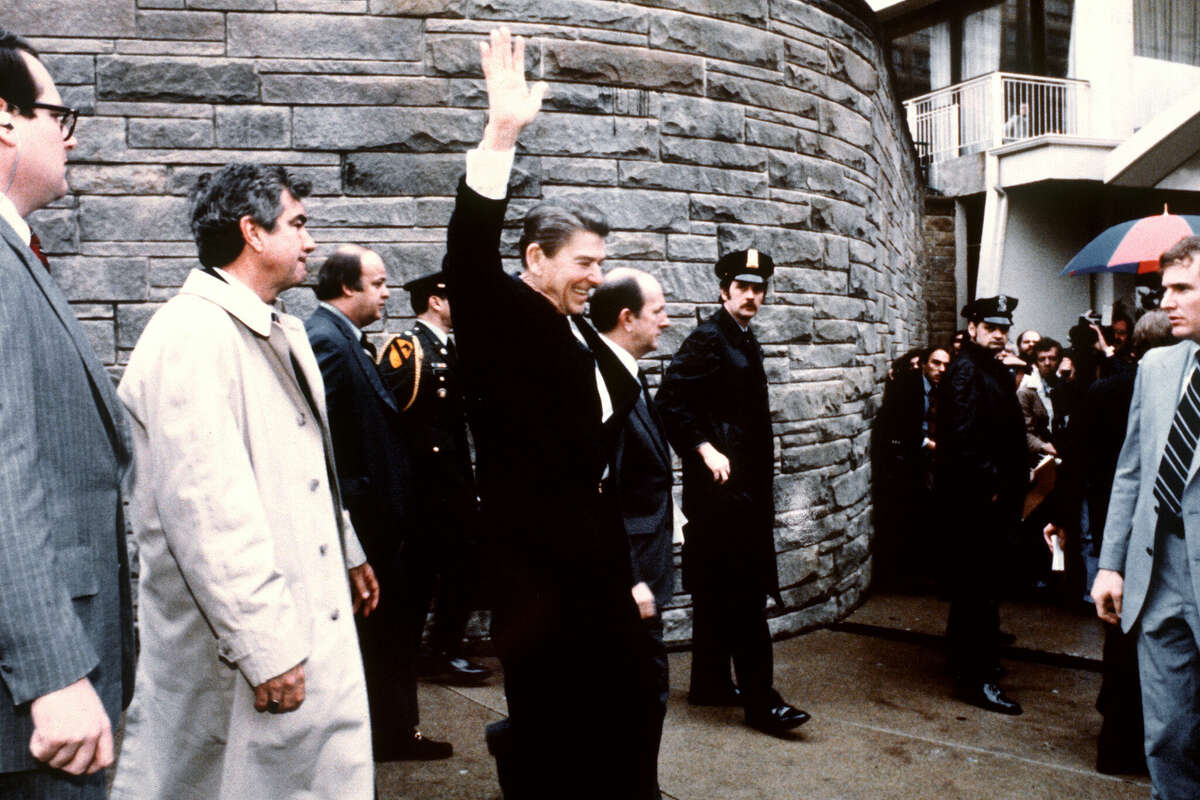 This photo taken by presidential photographer Mike Evens on March 30, 1981 shows President Ronald Reagan waving to the crowd just before the assassination attempt on him, after a conference outside the Hilton Hotel in Washington, D.C.. Reagan was hit by one of six shots fired by John Hinckley, who also seriously injured press secretary James Brady (just behind the car). Reagan was hit in the chest and was hospitalized for 12 days. Hinckley was aquitted 21 June 1982 after a jury found him mentally unstable. (Photo credit should read MIKE EVENS/AFP via Getty Images)