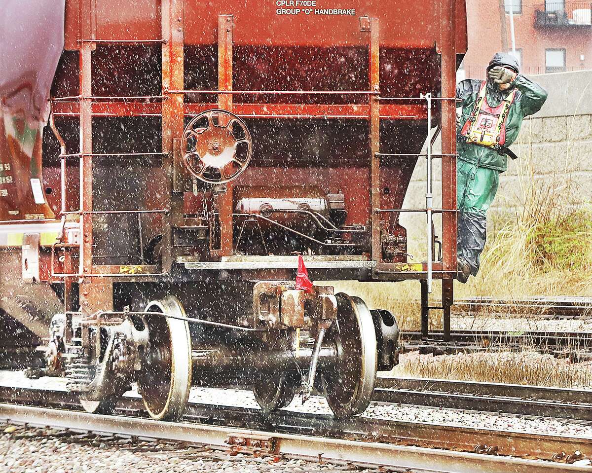 John Badman|The Telegraph A railroad worker covers his face from the blowing rain Wednesday as he rides the back of a hopper car on a train going backwards along the Alton riverfront. Scattered showers will continue into Thursday before clearing and warming into the 60s for the weekend.