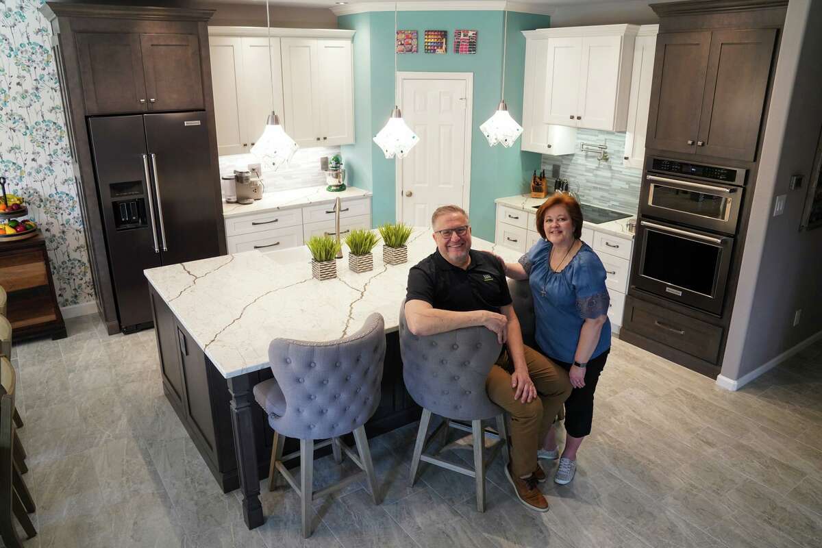 Penny and Don Wuebben pose before their newly renovated kitchen, which has a large, center island and white and slate cabinets.
