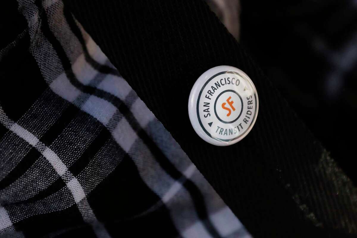 A person wears a San Francisco Transit Riders button after the ribbon cutting for the Van Ness BRT.