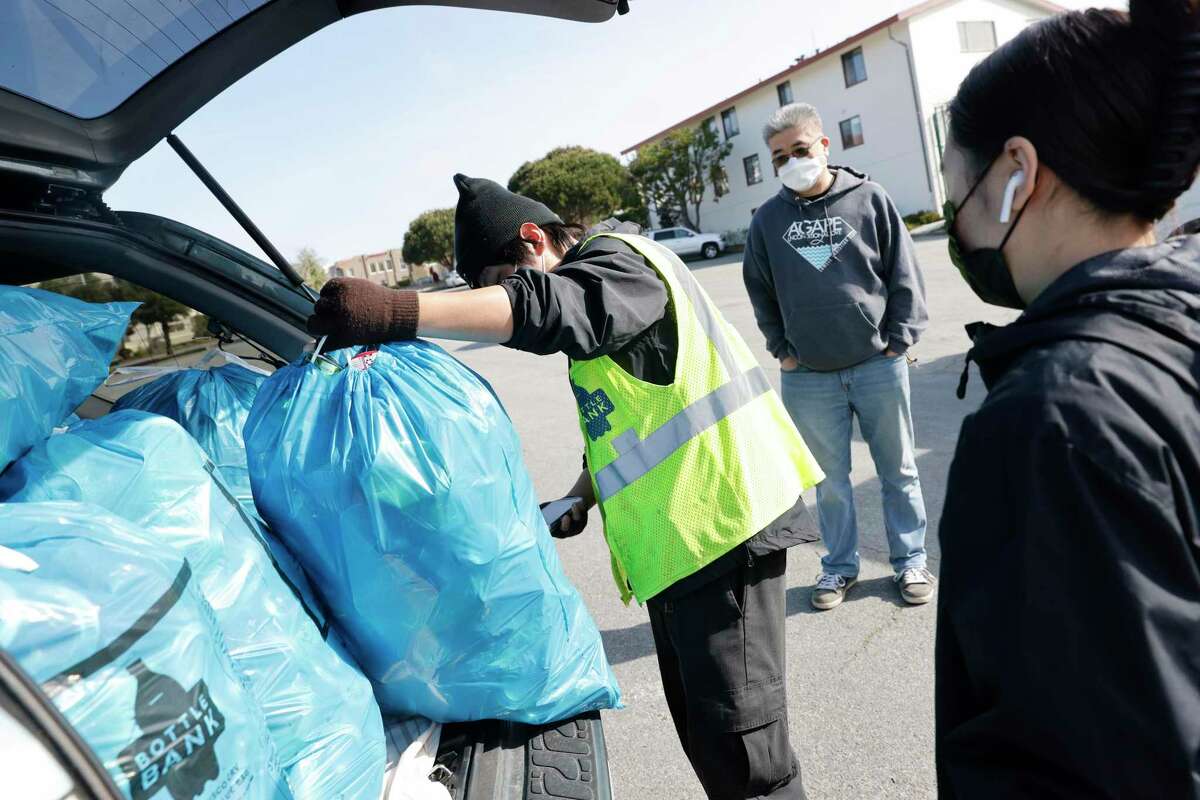 Leo Lee (left), crew lead, scans the UPC code on a blue bag of Wilson Sinn (center) of San Francisco, who was dropping off bags of recycling at the mobile drop-off location at Stonestownon Shopping Center on Thursday, March 31, 2022 in San Francisco, Calif.