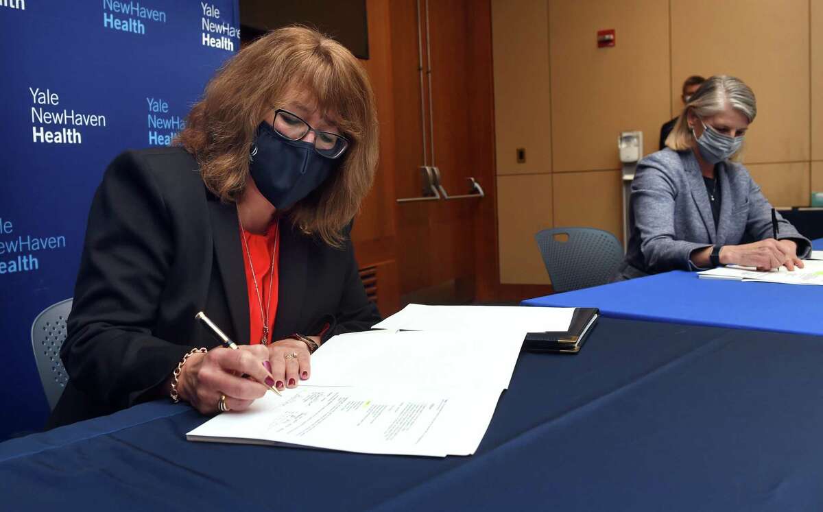 Lisa O'Connor (left), dean of the Quinnipiac University School of Nursing, and Sandra Bulmer, dean of the Southern Connecticut State University College of Health and Human Services, sign a nursing school partnership agreement at a press conference at Yale New Haven Hospital in New Haven on March 31, 2022. The nursing school partnership includes Yale New Haven Health, Fairfield University, Gateway Community College, Quinnipiac University and Southern Connecticut State University. Nursing is one of the key areas in which Yale New Haven Health and other health care providers in Connecticut have a significant number of positions to fill.