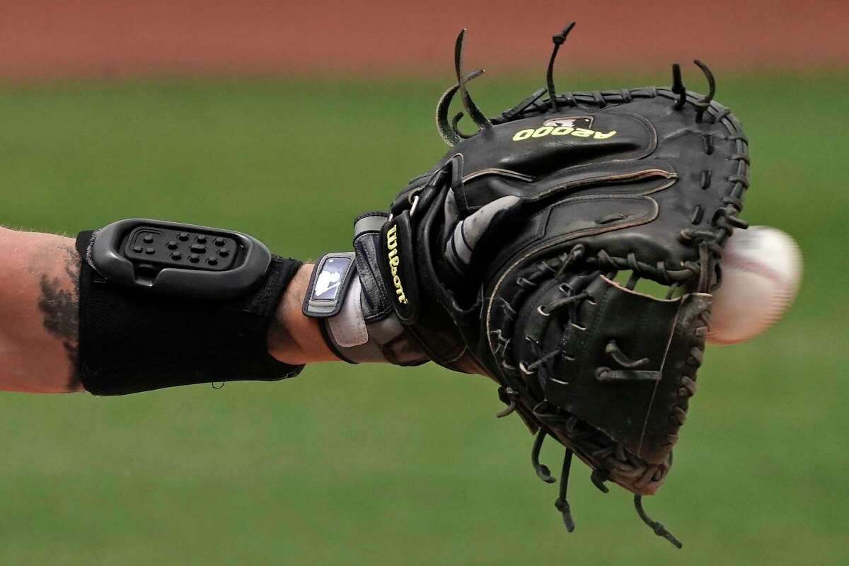 Seattle Mariners catcher Tom Murphy wears a wrist-worn device used to call pitches as he catches a ball during the sixth inning of a spring training baseball game against the Kansas City Royals, Tuesday, March 29, 2022, in Peoria, Ariz. The MLB is experimenting with the PitchCom system where the catcher enters information on a wrist band with nine buttons which is transmitted to the pitcher to call a pitch.