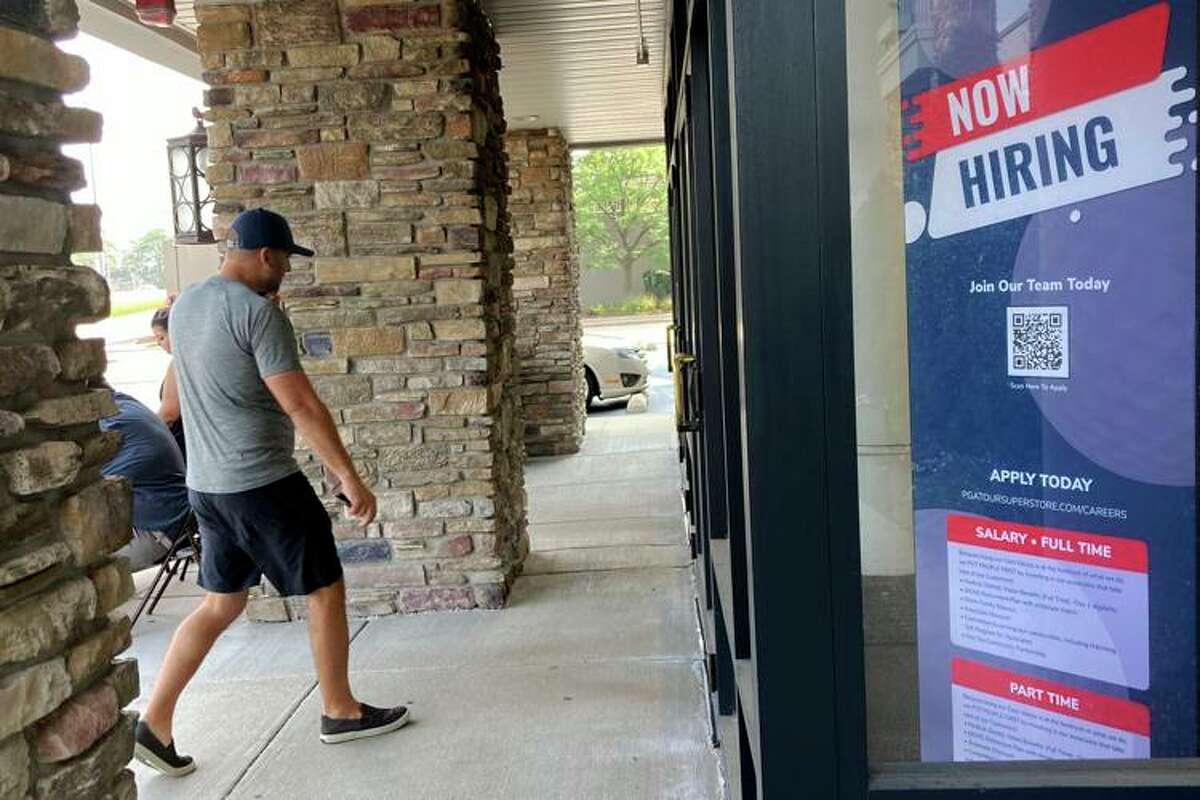 A man walks past a "now hiring" sign.