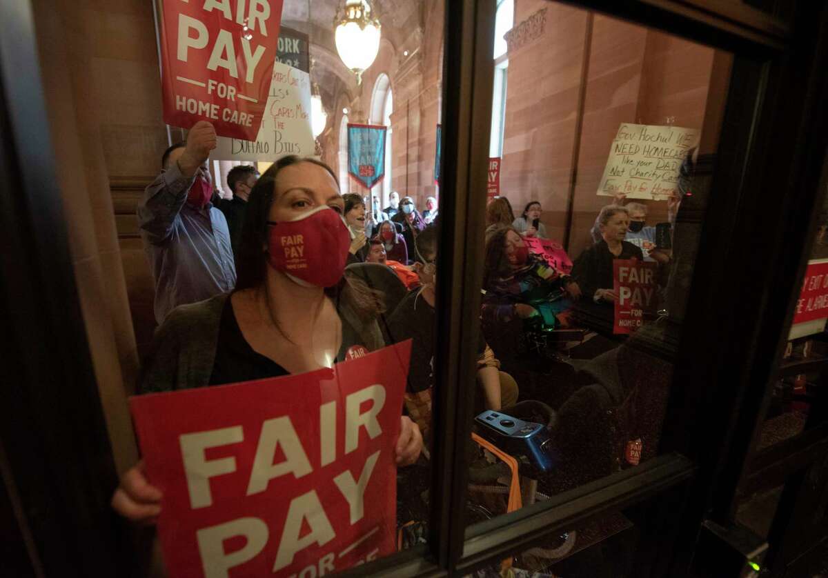 Demonstrators advocating for fair pay for home care are seen through a doorway to the Governor’s hallway at the New York State Capitol on Monday, April 4, 2022 in Albany, N.Y. Legislators and Governor Kathy Hochul are hoping to pass the budget soon. Wages for home health aides are set to increase by $3. 