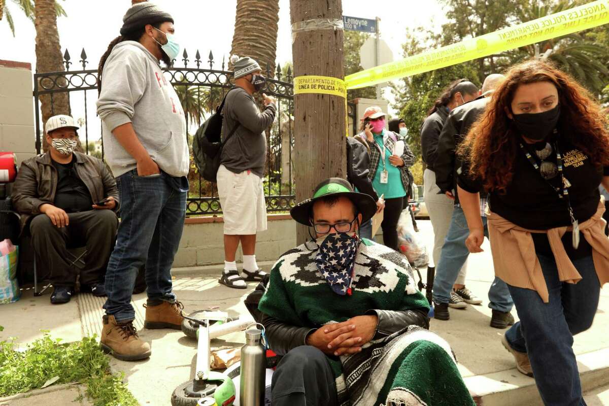 Homeless people who were evicted from their encampments in Echo Park wait for information for alternative housing across the street from the park in Los Angeles on March 25, 2021.