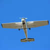 Light aircraft flying overhead at takeoff with blue sky.
