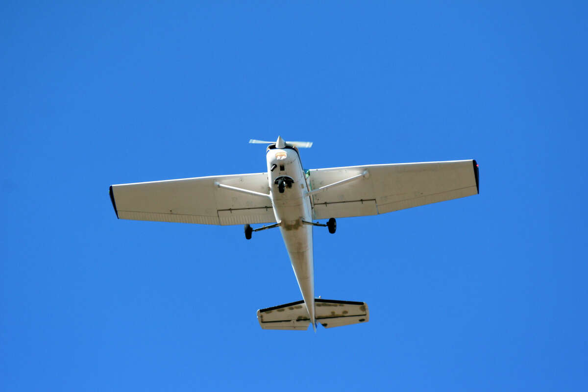 Light aircraft flying overhead at takeoff with blue sky.