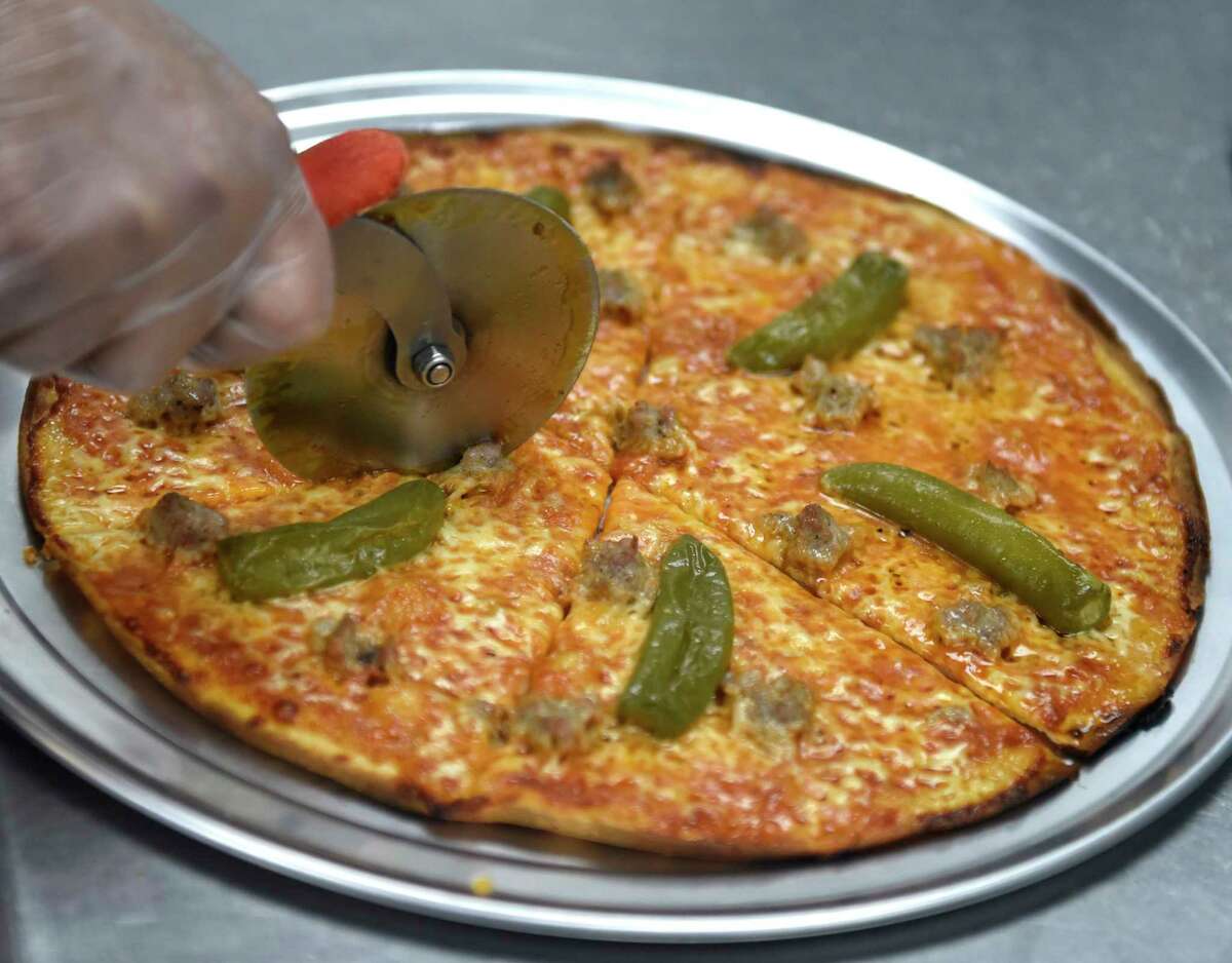 Eduardo Sanchez slices a stinger pepper and sausage pizza fresh out the oven during the opening day at Riko's Pizza in Stamford, Conn. Tuesday, April 5, 2022. Riko's Pizza opened a new location at 2010 West Main St. in Stamford on Tuesday. The menu features a variety of thin crust pizzas, including the famous hot oil pizza, as well as salad pizzas, hot wings, and a full bar with an innovative cocktail menu.