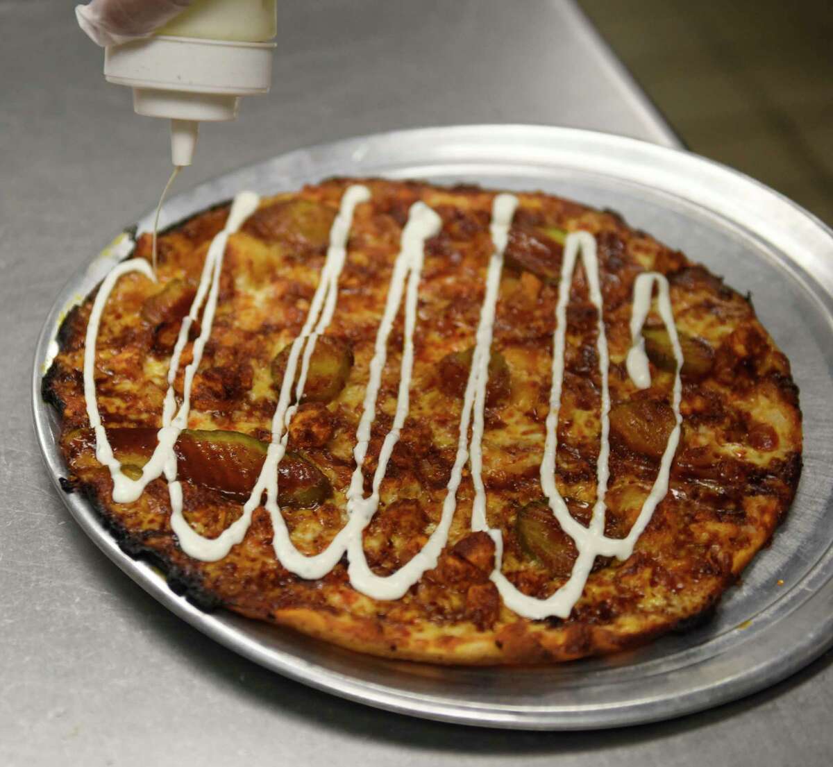 Eduardo Sanchez tops a hot Nashville chicken pizza with ranch dressing on opening day of Riko's Pizza in Stamford, Conn. on Tuesday, April 5, 2022. Riko's Pizza opened a new location at the 2010 West Main St. in Stamford.  The menu offers a variety of thin crust pizzas, including the famous hot oil pizza, as well as salad pizzas, hot wings and a full bar with an innovative cocktail menu.