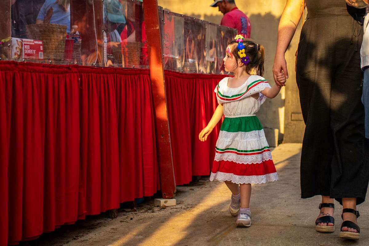 A girl passes by a grilled chicken stand set up in Chinatown at A Night in Old San Antonio on Tuesday, April 5, 2022. The four-night festival, called NIOSA for short, traditionally draws about 85,000 people to downtown’s La Villita.