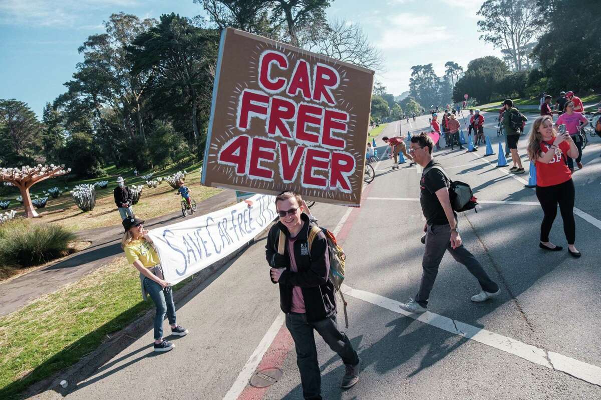 Greg Rozmarynowycz carries a large sign at the start of a “Save JFK” rally on JFK Drive in Golden Gate Park on Saturday, February 12, 2022. Members of Walk SF organized the “Save JFK” rally to garner support in an effort to keep JFK Drive car free.