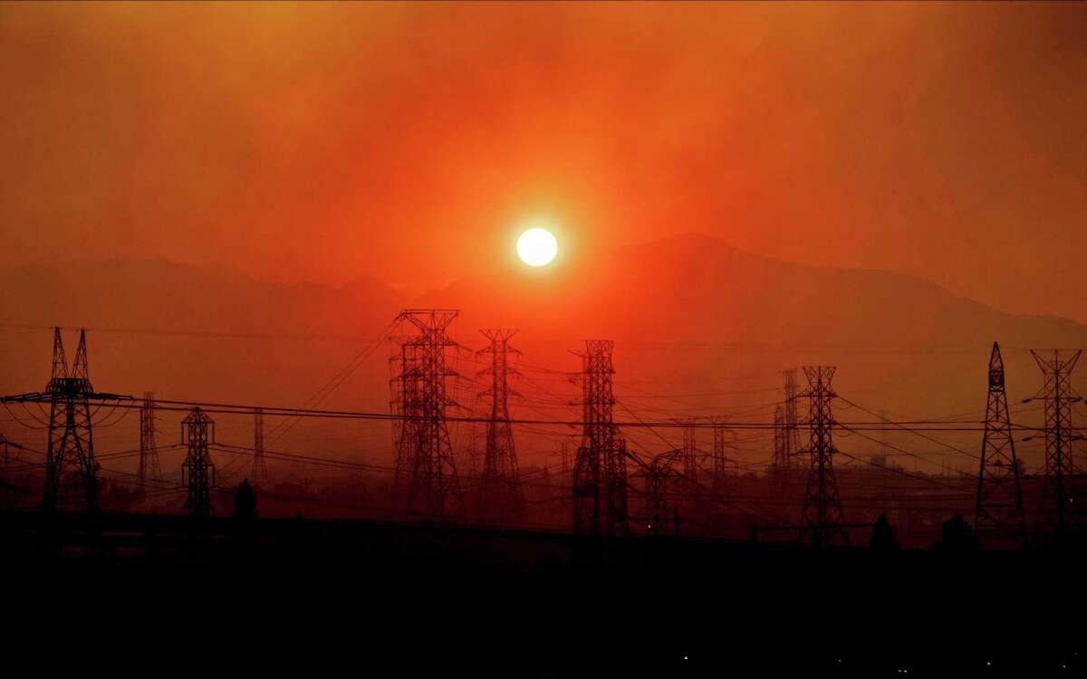 Smoke from a wildfire called the Saddle Ridge Fire hangs above power lines as the sun rises in Newhall, Calif. Weather disasters fueled by climate change now roll across the U.S. year-round, battering the nation's aging electric grid.