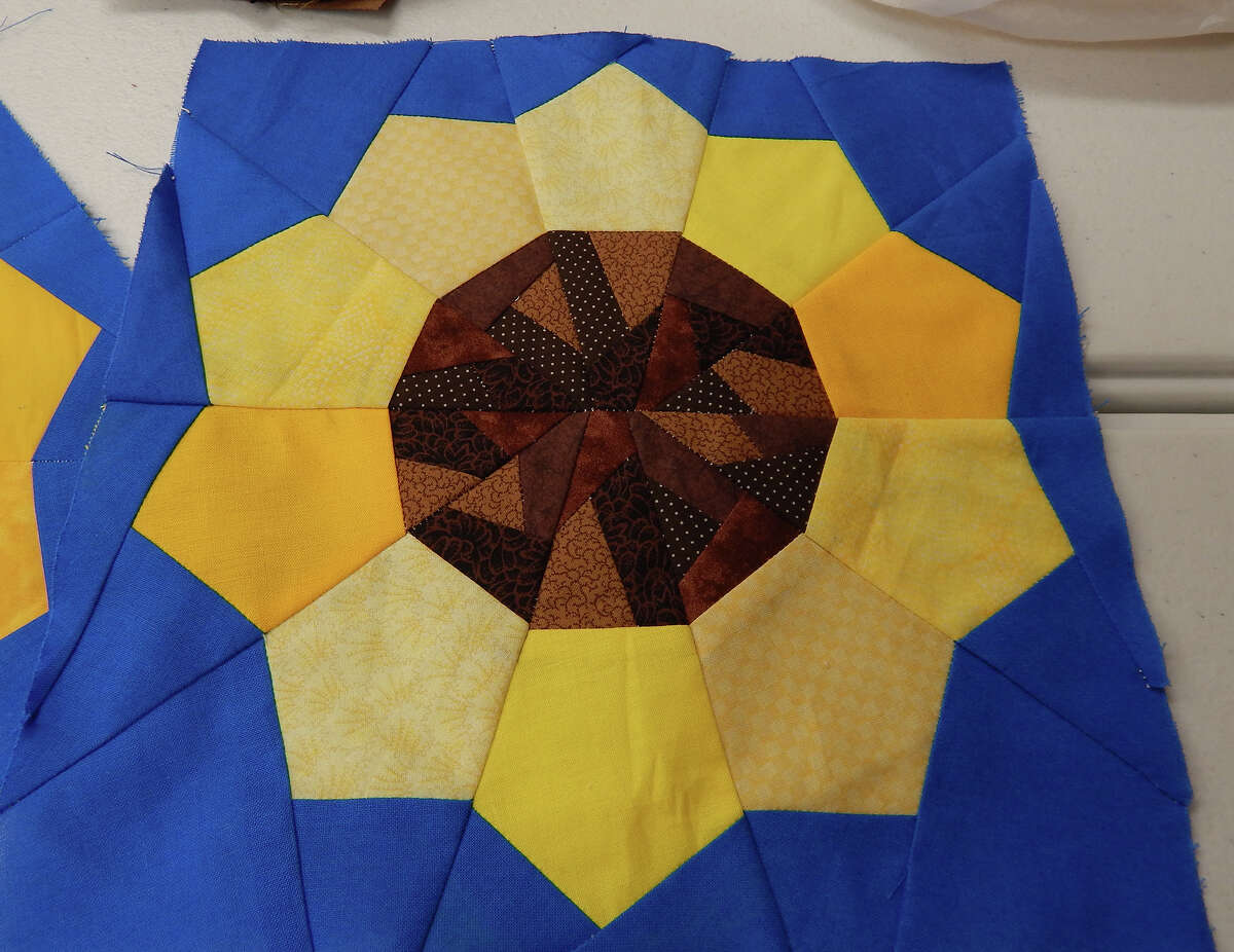 A Sunflowers of Ukraine quilt block is paper-pieced using scraps of yellow, brown and blue fabric. Quilters are asked to provide their own yellow and brown fabrics, though the blue is provided so it will help unify the various blocks.