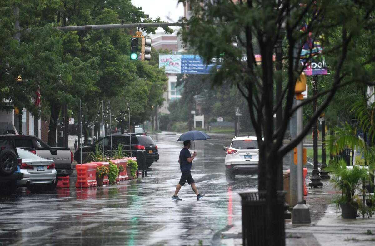 A pedestrian crosses the street with an umbrella as Tropical Storm Henri hits Stamford, Conn. Sunday, Aug. 22, 2021. Henri was downgraded from a hurricane to a tropical storm as the storm took a turn eastward before hitting land.