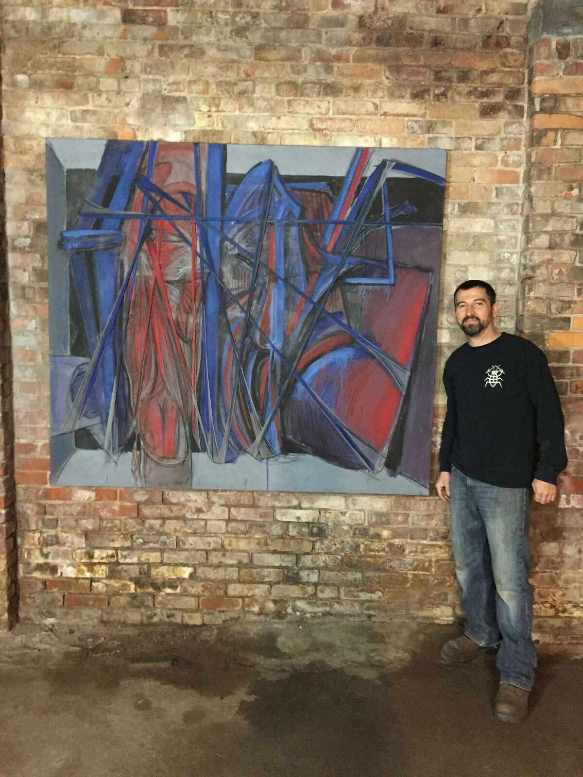 Jared Whipple, a car mechanic from Waterbury who found a large art collection from Francis Hines in a dumpster in Watertown, standing in front of Hines' painting. 