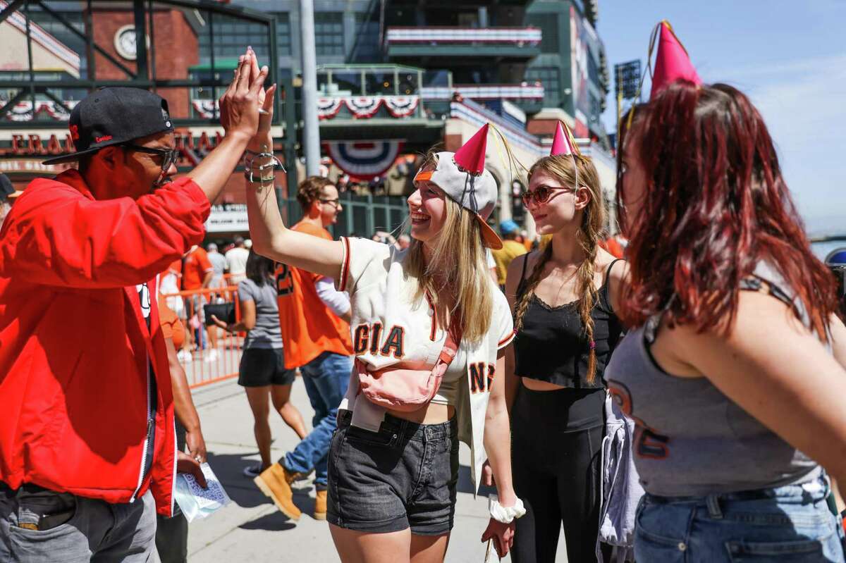 Kaia Kottmeier, 16,(center) high-fives a man outside of Oracle Park ahead of Giants opening day on Friday, April 8, 2022 in San Francisco, California.