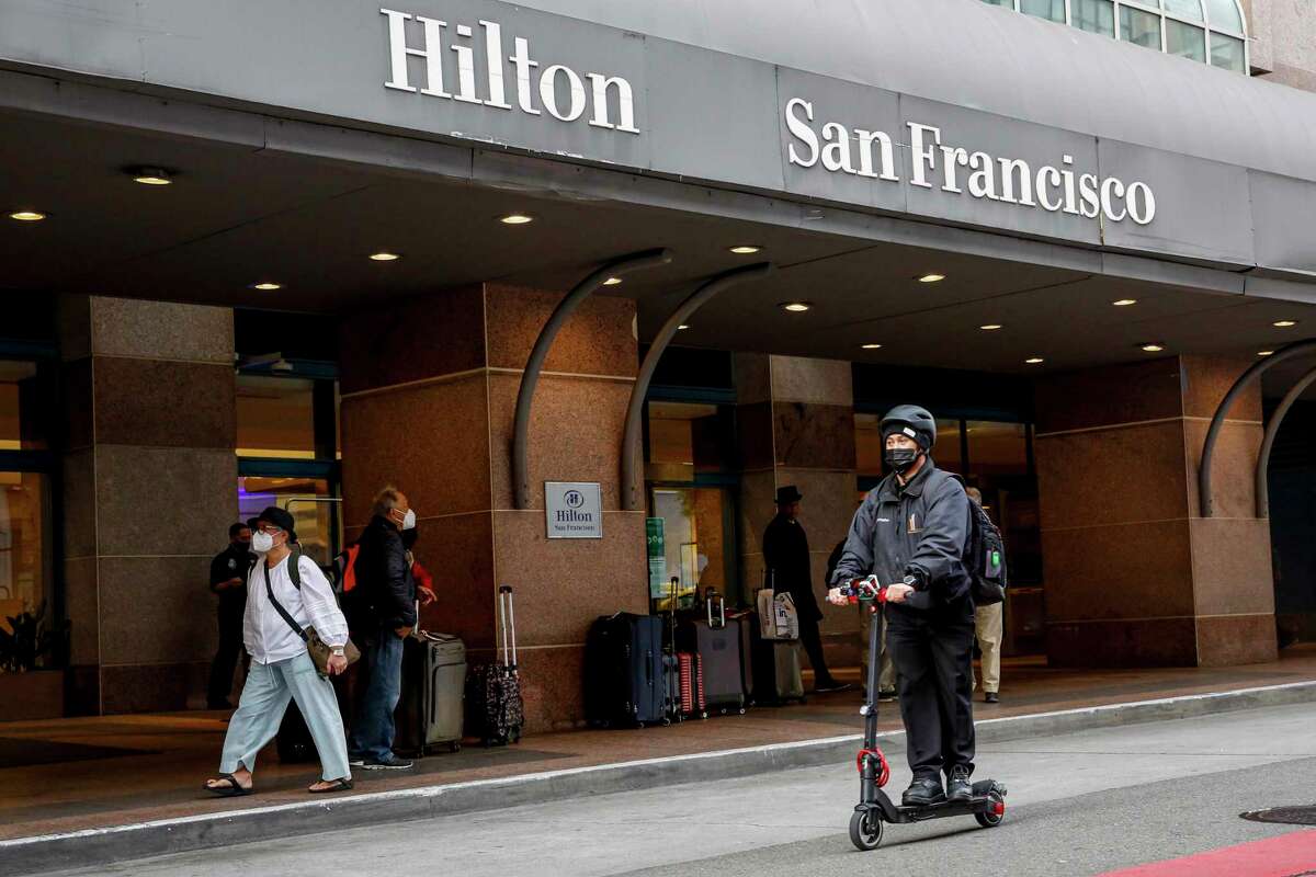 Christopher Flores rides a scooter past the Hilton on his way home from working a graveyard shift as a parking lot attendant. Flores was furloughed from the Hilton at the height of the pandemic, and still has not been asked to return full time.