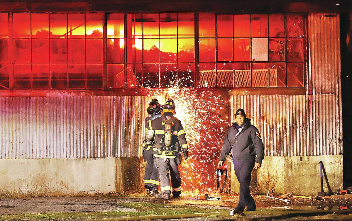 John Badman|The Telegraph Alton firefighters use a saw to cut through the steel door of the warehouse at 9th and Piasa in Alton late Friday night as fire, above, burns inside the structure. No injuries were reported. 