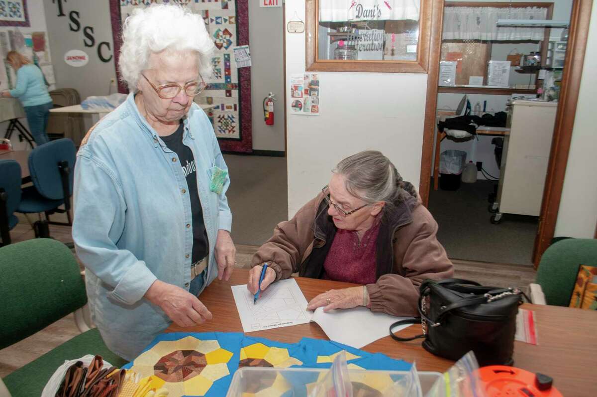 LaVern Roy (left) shows Pat Martin how to make a sunflower quilt block Saturday at Time Square Sewing Complex. The blocks will used for placemats or wall hangings and sold to benefit the children of Ukraine.