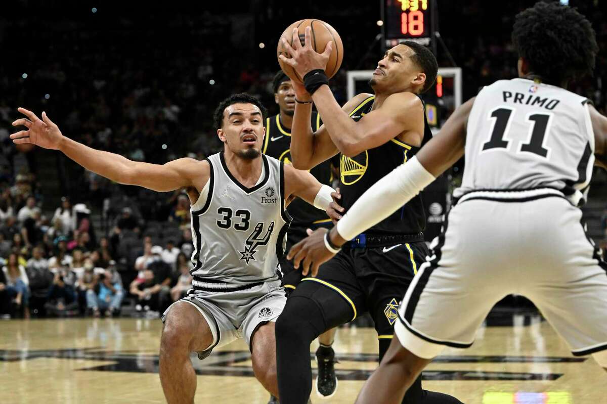 Golden State Warriors' Jordan Poole, center, tangles with San Antonio Spurs' Tre Jones (33) and Josh Primo during the first half of an NBA basketball game on Saturday, April 9, 2022, in San Antonio. (AP Photo/Darren Abate)