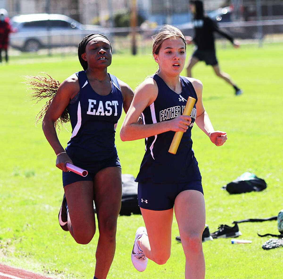 Father McGivney's Kaitlyn Hatley (right) leads Belleville East's Bria Johnson on the opening lap of the 4x800 relay on Saturday at the EA-WR Invitational at Memorial Stadium in Wood River. McGivney won in a school-record time of 9:55.55.