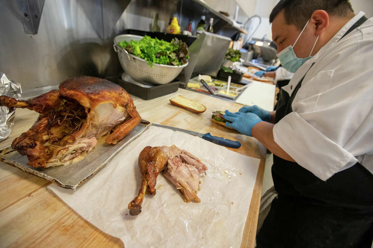An employee cuts pieces of turkey to make a hot roasted turkey sandwich at Arguello Market in San Francisco on April 10, 2022.