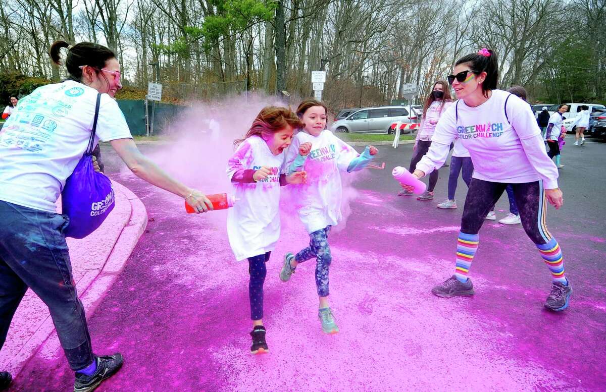 Alessandra Letts, left, and Emily Brahms, right, spray color dust onto passing participants during the fifth annual Greenwich Color Challenge at the International School at Dundee in Greenwich on Saturday. The 1.5-mile course began and finished at the ISD fields and took participants through obstacles, a foam pit and color stations where kids and adults got dusted with safe and washable powder as they ran past.