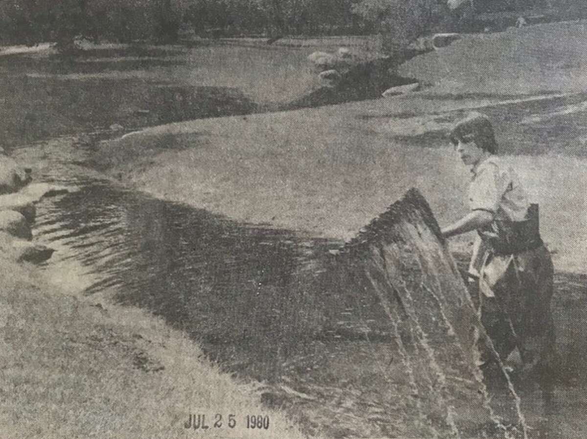 Sue Applegath, a summer employee at Dow Gardens, rakes the stream that winds through the gardens. July 1980