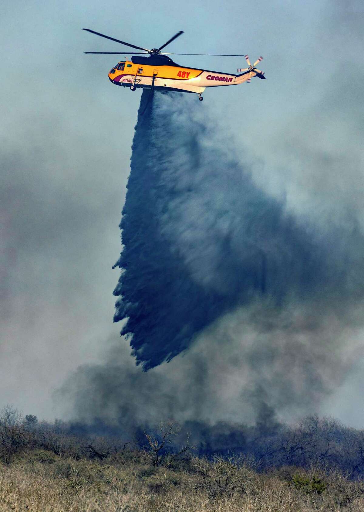 A helicopter drops water Tuesday, March 15, 2022, on a wildfire south of Jourdanton in Atascosa County. In addition to area fire departments on the ground, the Texas Forest Service used the helicopter and two large tankers to fight the fire.