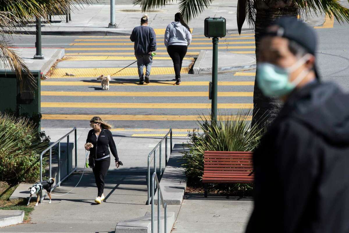 A combination of masked and maskless pedestrians walk through Dolores Park in San Francisco, Calif. Friday, March 4, 2022.