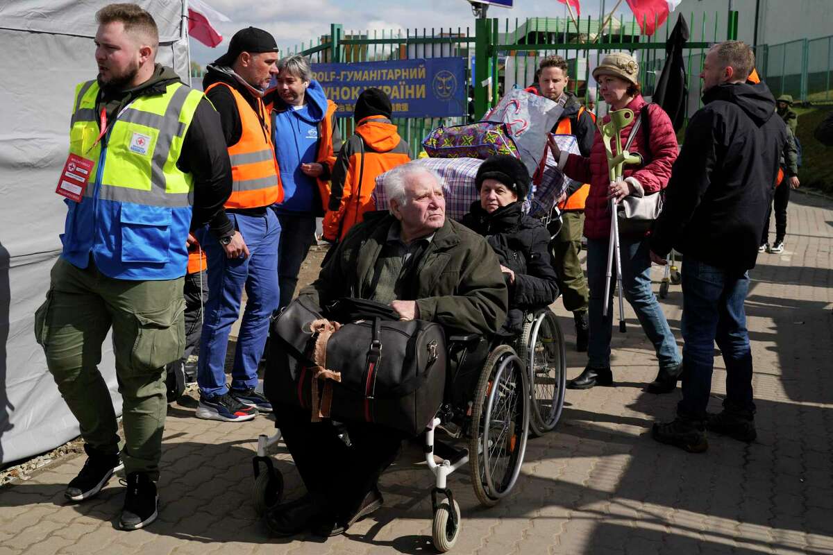 Volunteers help refugees in a wheelchair after fleeing the war from neighboring Ukraine at the border crossing in Medyka, southeastern Poland, Monday, April 11, 2022.