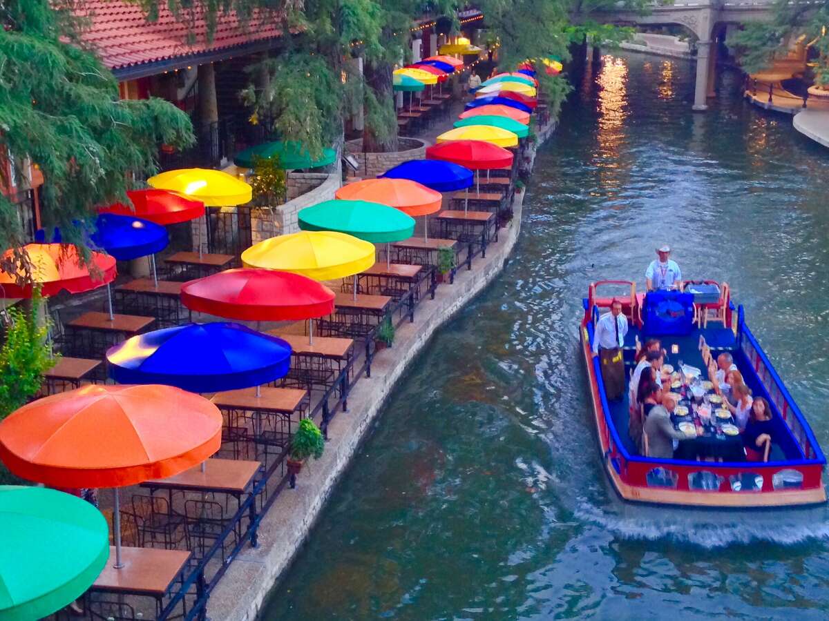 An electric tour boat cruises along the banks of the San Antonio River Walk.