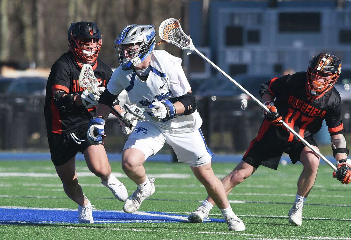 Darien’s Tighe Cummiskey, center, comes up with the ball during a faceoff in front of Ridgefield’s Chris Reinhardt, left, and Liam Gerosa during a boys lacrosse game on Tuesday in Darien.