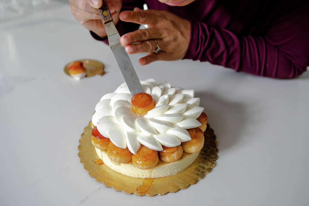 Monique Feybesse places a choux puff onto a St. HonorŽ Tart in her home kitchen in Vallejo, Calif. on April 8, 2022. Monique and her husband Paul bake all the pastries and breads created by their company Tarts de Feybesse themselves.