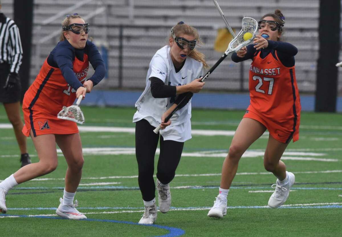 Darien’s Ryan Hapgood splits Manhasset defenders Ashley Newman, left, and Despina Giannakopoulos during a girls lacrosse game on Wednesday, April 6, 2022 in Darien, Conn.