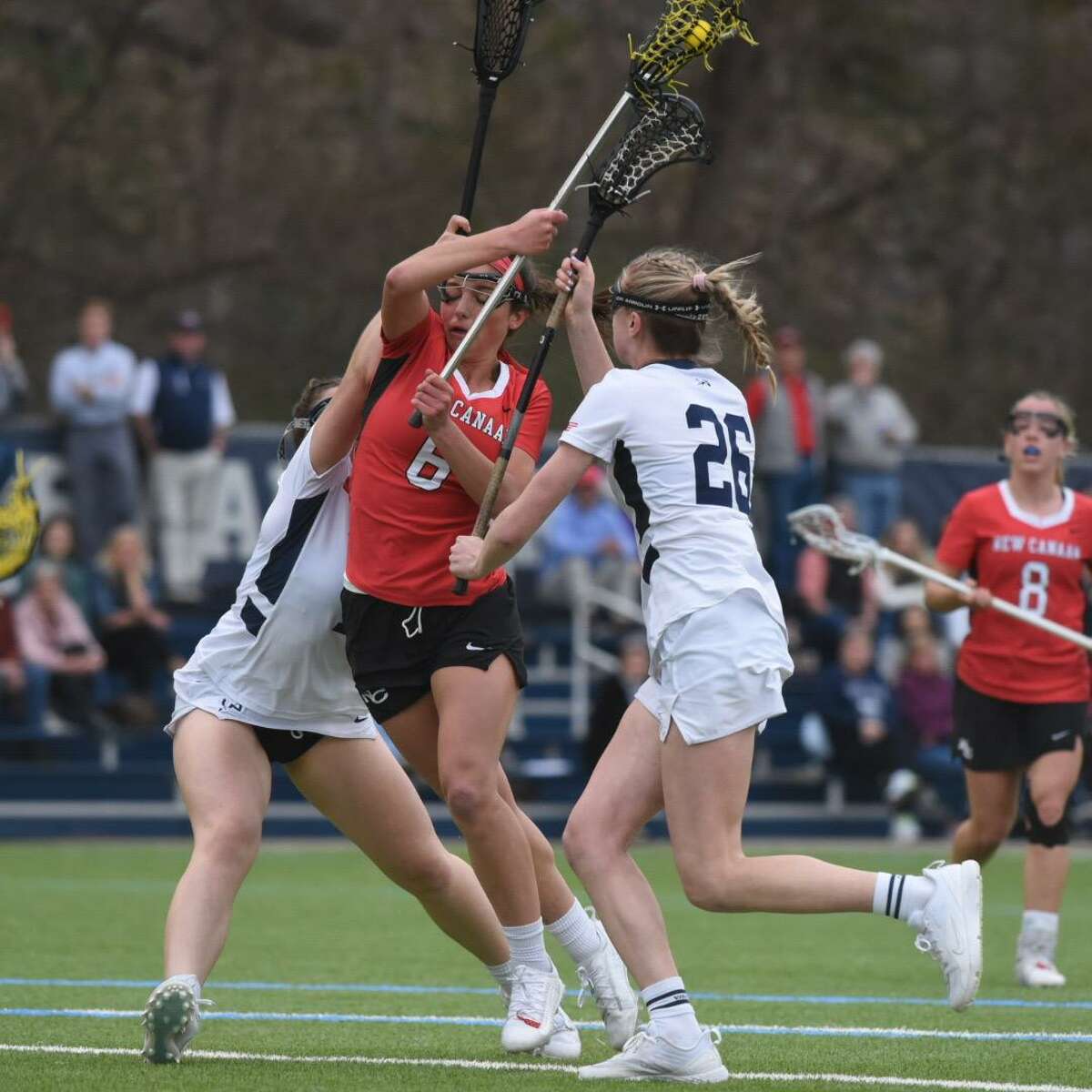 New Canaan’s Kaleigh Harden (6) tries to split a pair of Wilton defenders, including Ashleigh Masterson (26) during a girls lacrosse game on Wednesday, April 13, 2022 in Wilton, Conn.