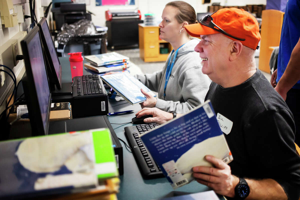 Tracy Williams, left, and Bill Phillips, right, catalog books while working alongside a team of volunteers from Corteva and United Way of Midland County to help repurpose a space inside Meridian Elementary School and turn it into a multi-purpose library Thursday, April 14, 2022 in Sanford.