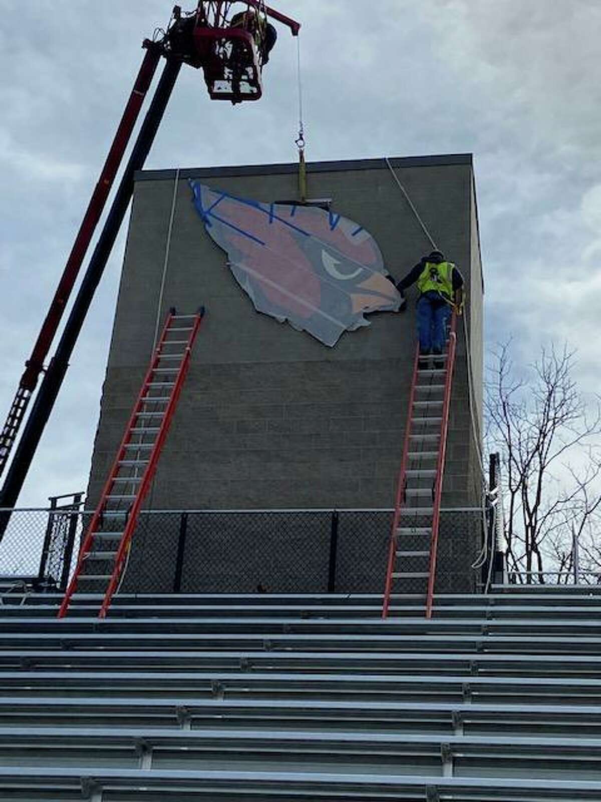 A cardinal logo is put in place above the bleachers at Greenwich High School's Cardinal Stadium Monday, April 11, 2022.